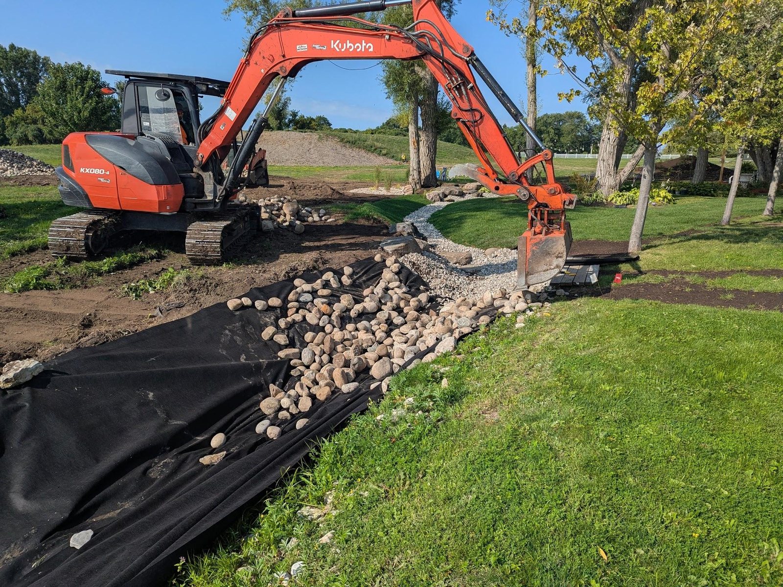 A Kubota excavator placing stone along the newly cut course of a creek