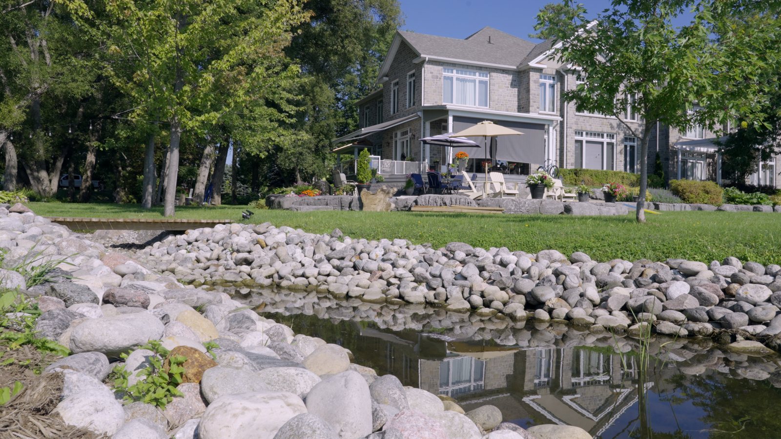 Large stone edging along the creek with the waterfront home reflected in the water