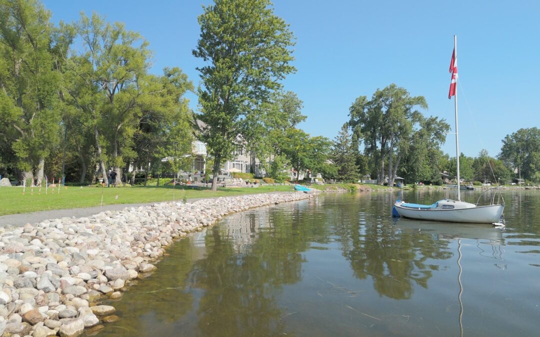 Stone-edged shoreline on the Bay of Quinte with a sailboat moored offshore and a Canadian flag flying